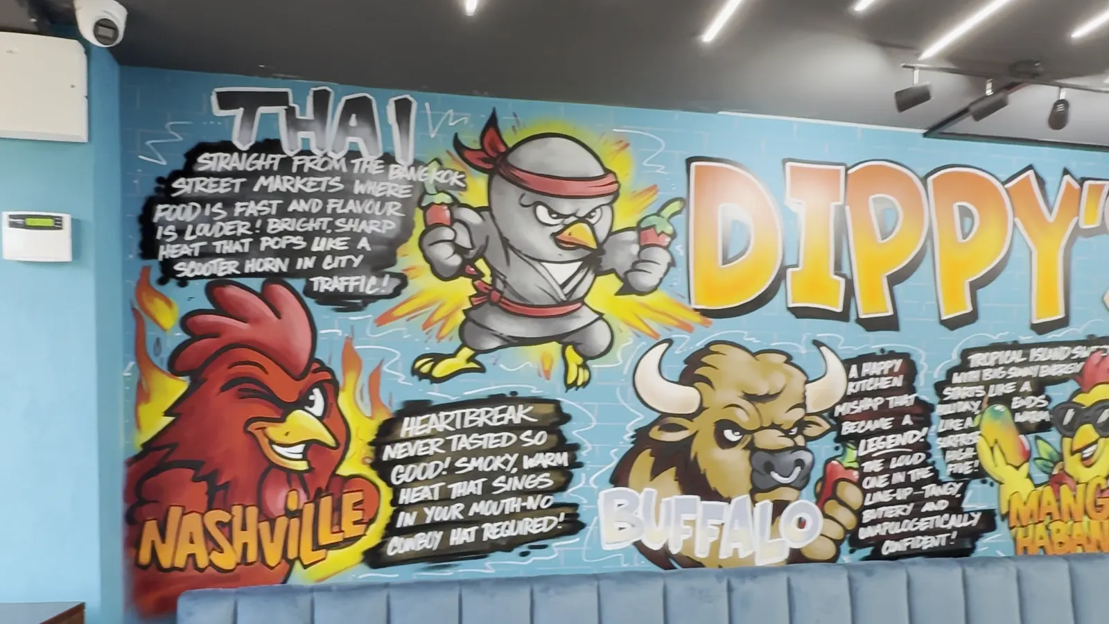 Hand-painted wall: the Thai Wave ninja, Nashville rooster and Buffalo bison with their stories, above teal booth seating