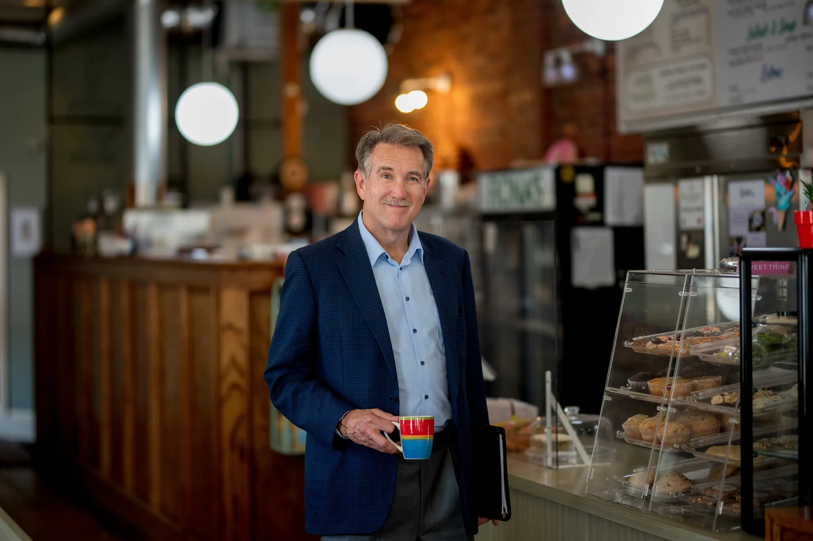 Don Scott photographed in a cafe, holding a coffee cup, in a navy blazer